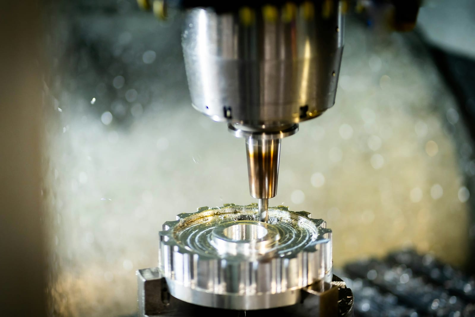 CNC 銑床主軸正在切削一個齒輪狀的鋁件，冷卻液噴灑中的淺景深特寫